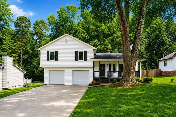 White siding exterior with a two-car garage, covered porch, and mature trees