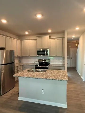 Kitchen featuring a central island with an undermount sink, stainless steel appliances, light-toned cabinetry, and wood-finish flooring