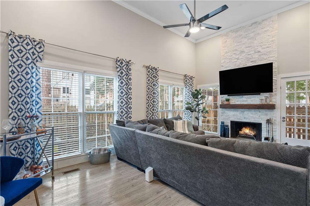 Living room featuring a stone fireplace, a towering ceiling, crown molding, ceiling fan, and light hardwood / wood-style flooring