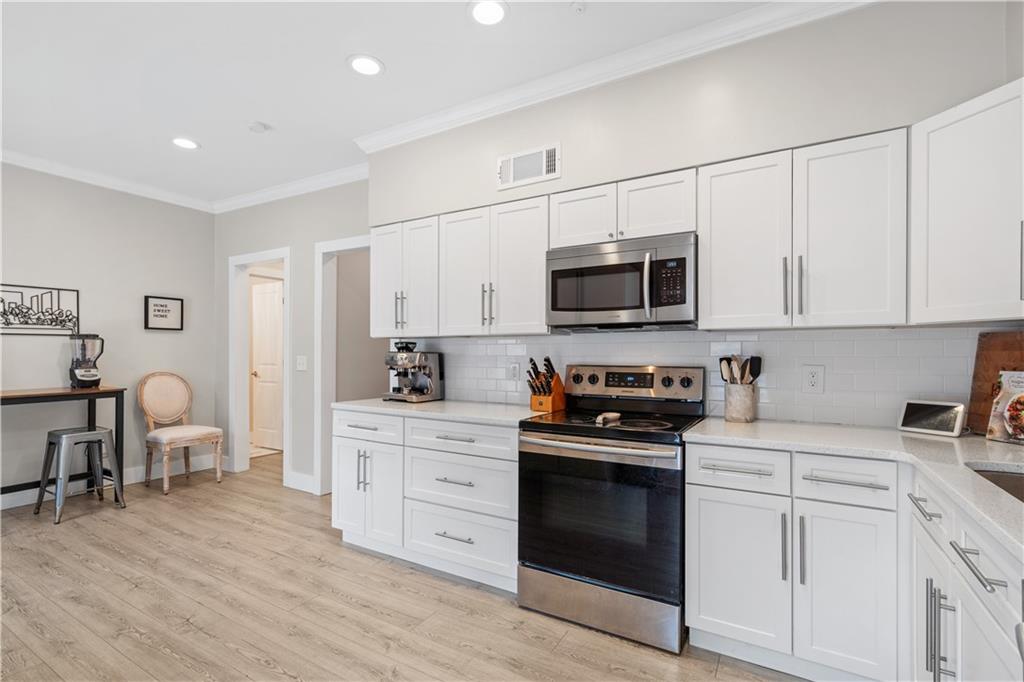 Kitchen with tasteful backsplash, stainless steel appliances, white cabinets