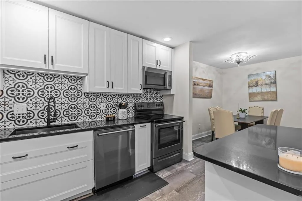 Kitchen with stainless steel appliances, white cabinets, backsplash, dark stone counters, and recessed lighting