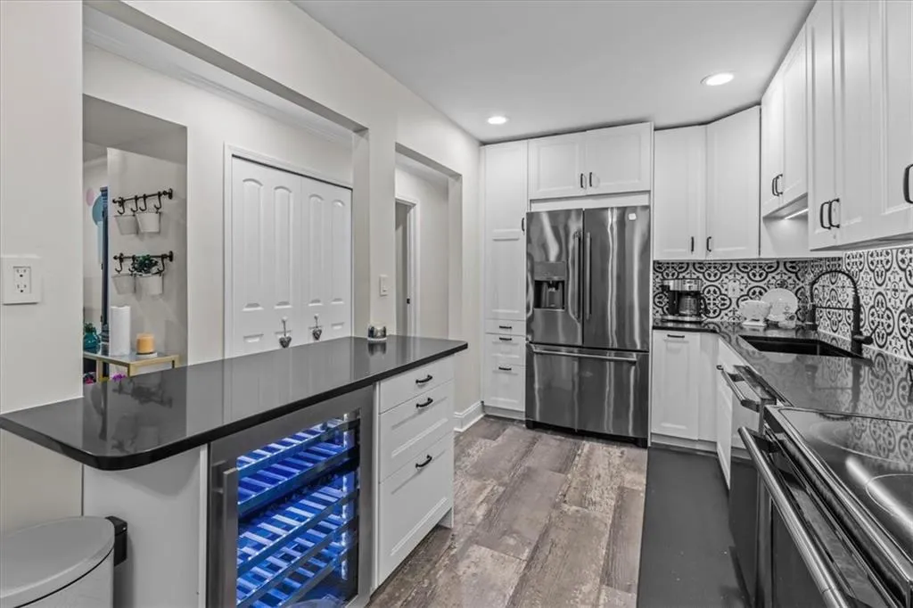Kitchen with beverage cooler, appliances with stainless steel finishes, white cabinetry, and recessed lighting
