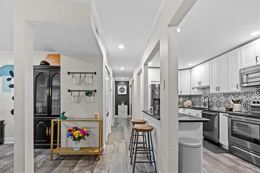 Kitchen featuring stainless steel appliances, white cabinets, light wood-style flooring, backsplash, and a breakfast bar area
