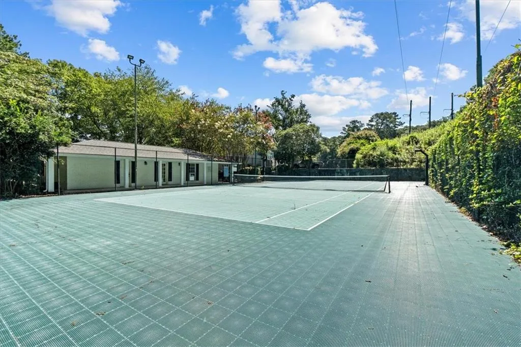 View of tennis court featuring view of wooded area