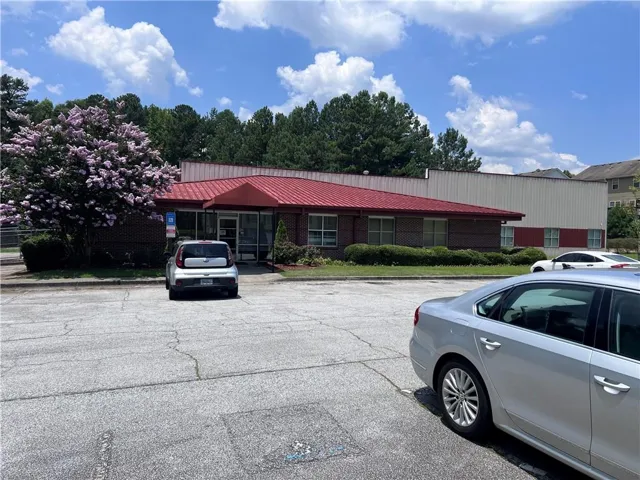 Single-story commercial building with brick facade and a red roof, featuring a paved parking area