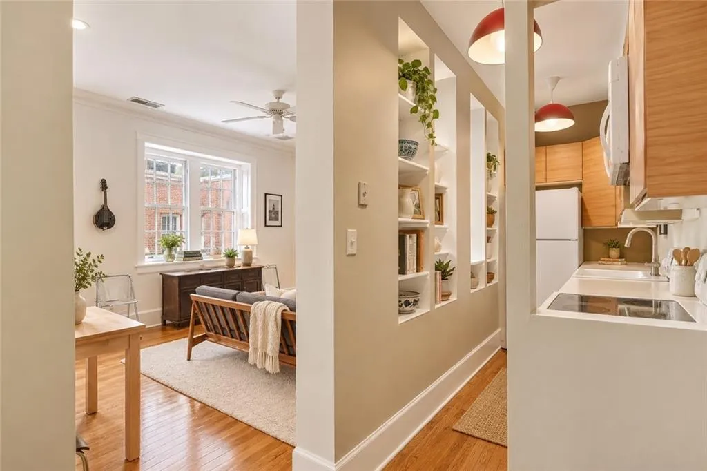 Just beyond the front door, original hardwood floors and thoughtful architectural details set the tone. Open shelving creates visual interest while maintaining a seamless connection between the entry, kitchen, and living spaces, allowing natural light to flow throughout the home. Staging digitally edited.