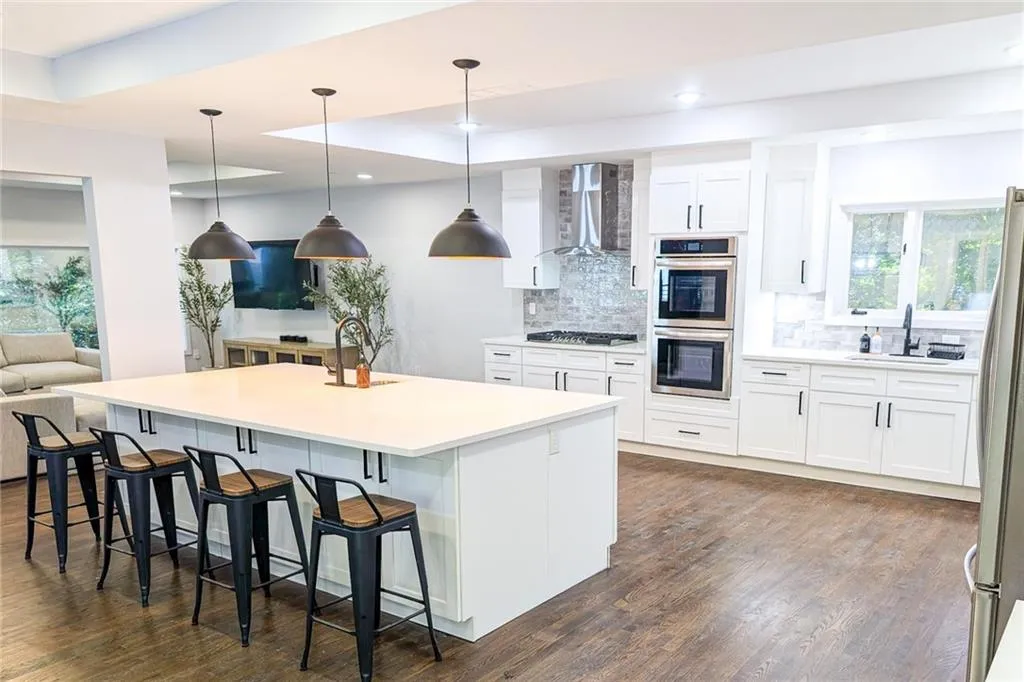 Kitchen featuring white cabinetry, a kitchen bar, tasteful backsplash, a kitchen island with sink, and decorative light fixtures