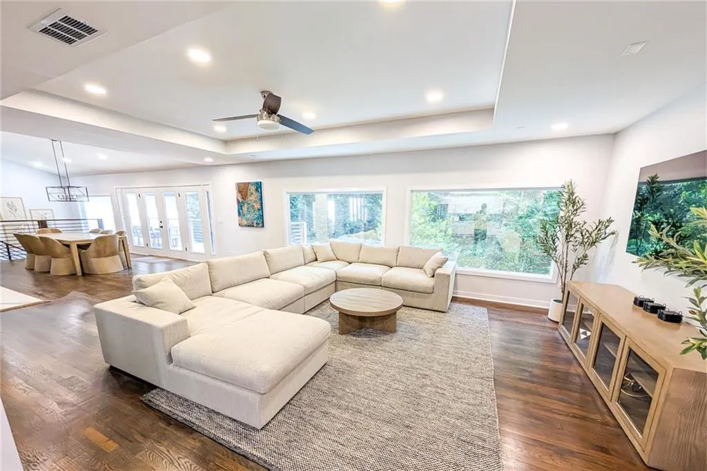 Living room featuring a raised ceiling, dark wood-type flooring, recessed lighting, and a ceiling fan