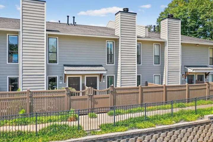 Exterior features a gray siding facade, multiple tall chimneys, and a brown privacy fence