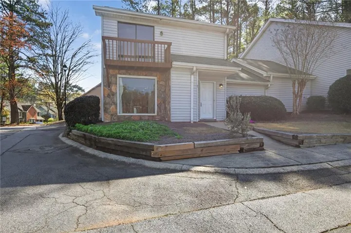 Stone facade accent, upper-level balcony, siding exterior, mature landscaping, and an inviting entry