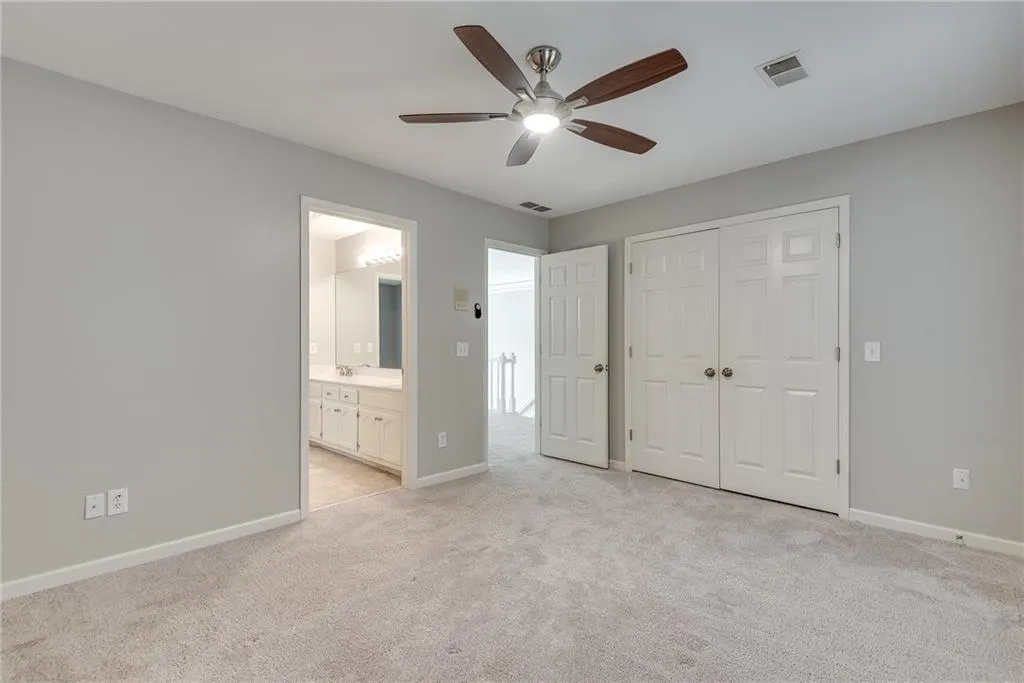 Unfurnished bedroom featuring light carpet, ensuite bathroom, a closet, and ceiling fan