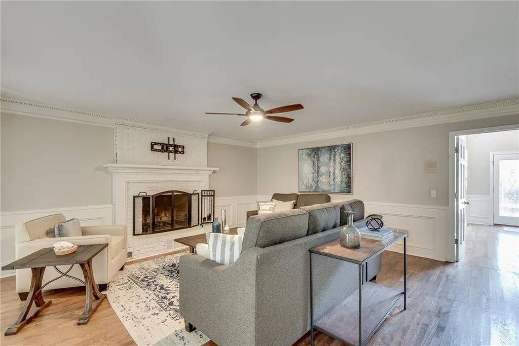 Living room with hardwood / wood-style flooring, a fireplace, brick wall, ceiling fan, and ornamental molding