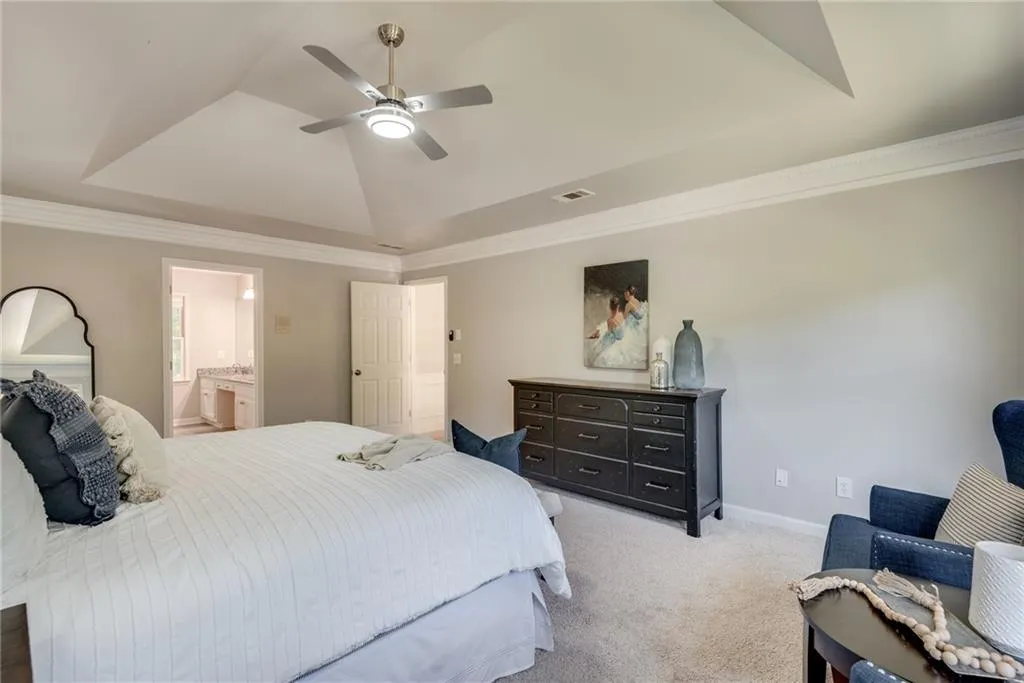 Carpeted bedroom with connected bathroom, ceiling fan, a raised ceiling, and ornamental molding