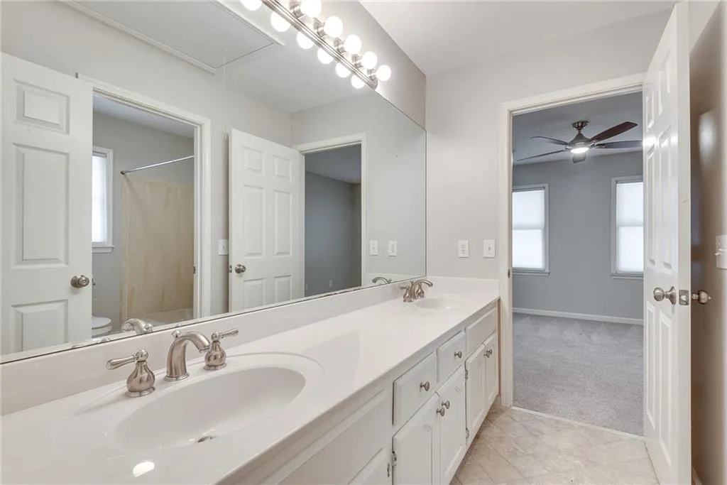 Bathroom with tile floors, vanity with extensive cabinet space, ceiling fan, toilet, and dual sinks