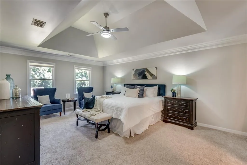 Carpeted bedroom featuring ceiling fan, a tray ceiling, and ornamental molding