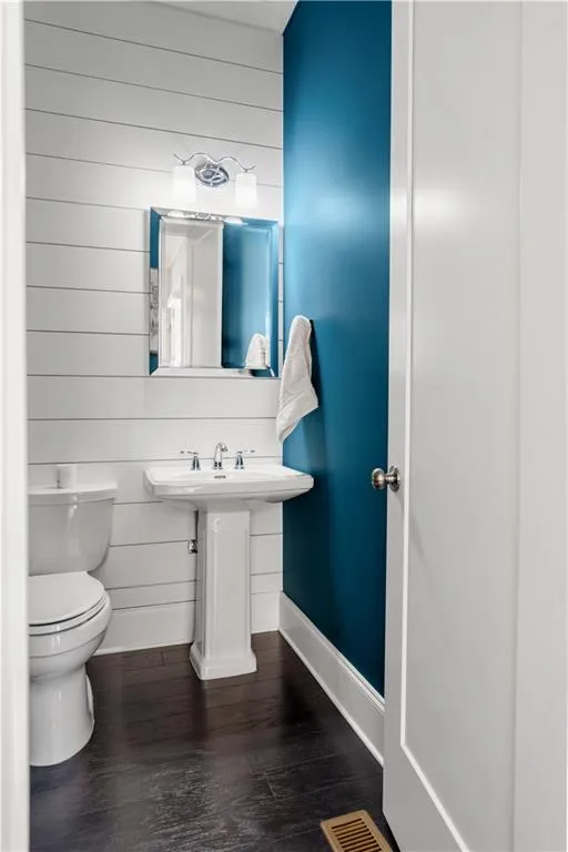 Half bathroom with visible vents, baseboards, toilet, and wood finished floors