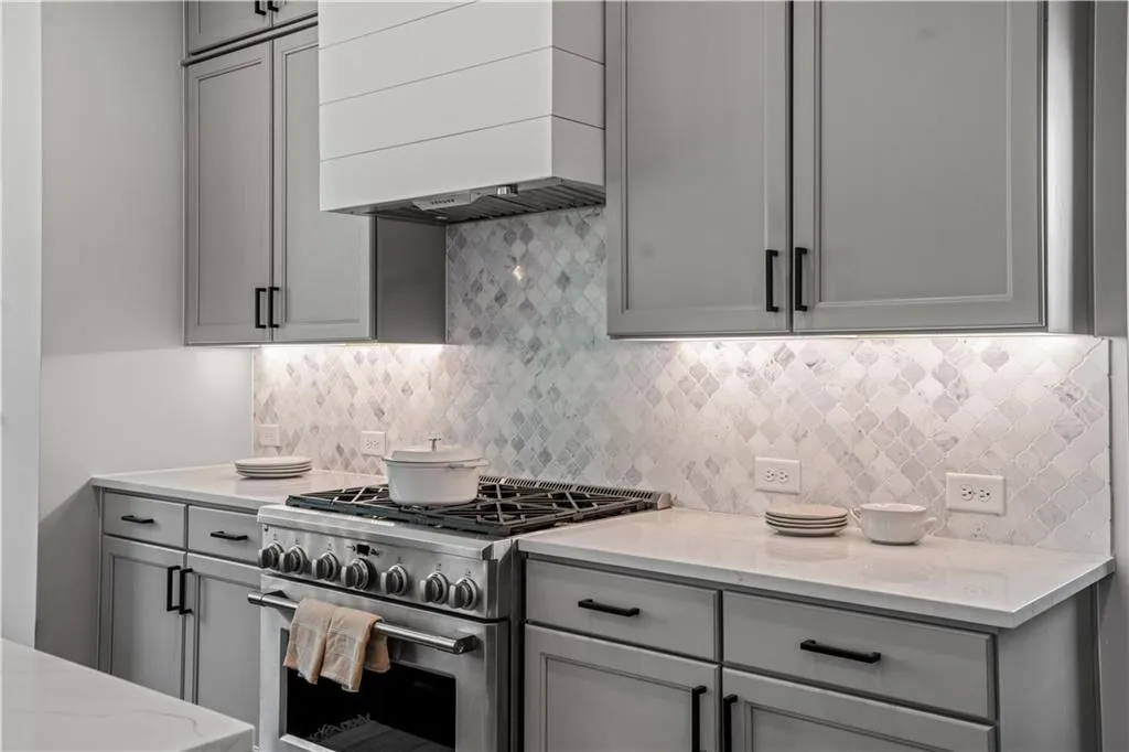 Kitchen with high end range, wall chimney exhaust hood, backsplash, and gray cabinets