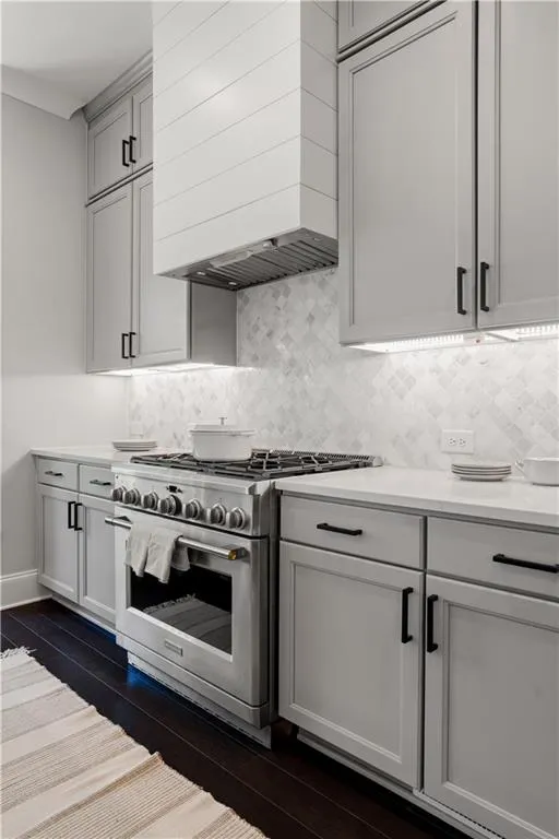 Kitchen with high end stainless steel range oven, wall chimney range hood, light countertops, backsplash, and dark wood finished floors