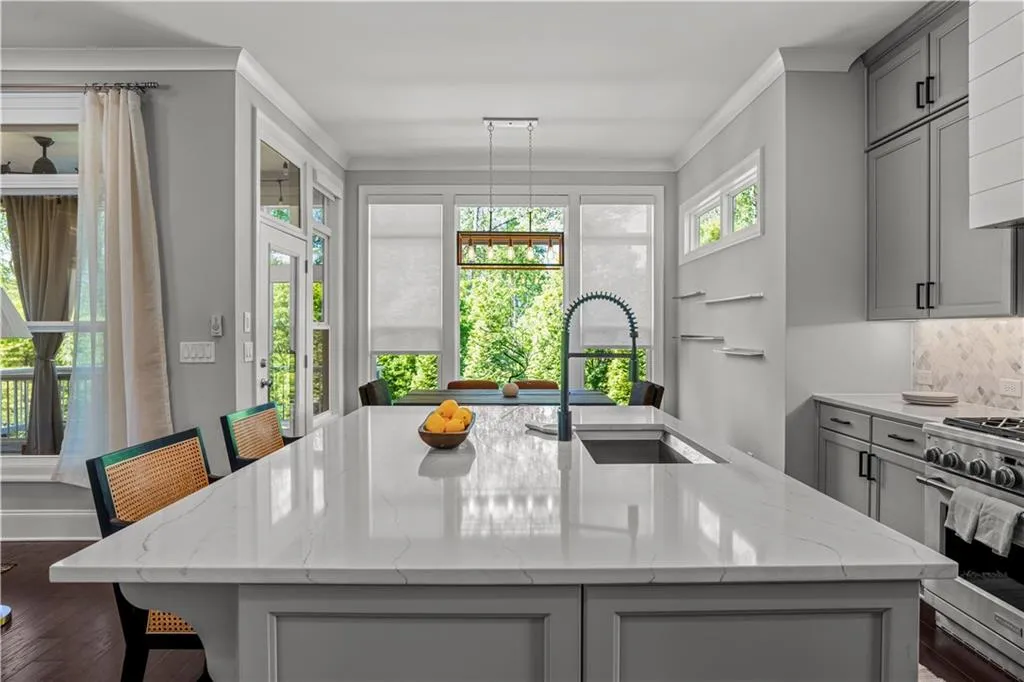 Kitchen featuring crown molding, an island with sink, stainless steel gas range, a sink, and gray cabinetry