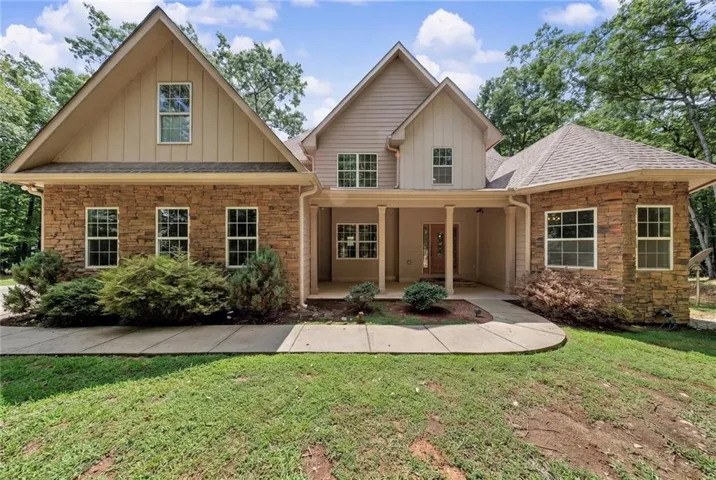 Exterior featuring stone veneer and vertical siding, a covered entry with columns, multiple windows, and a gabled roofline