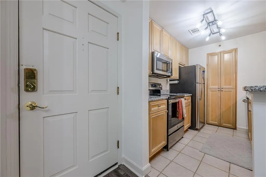 Kitchen with stainless steel appliances, light tile patterned flooring, light stone countertops, and light brown cabinets