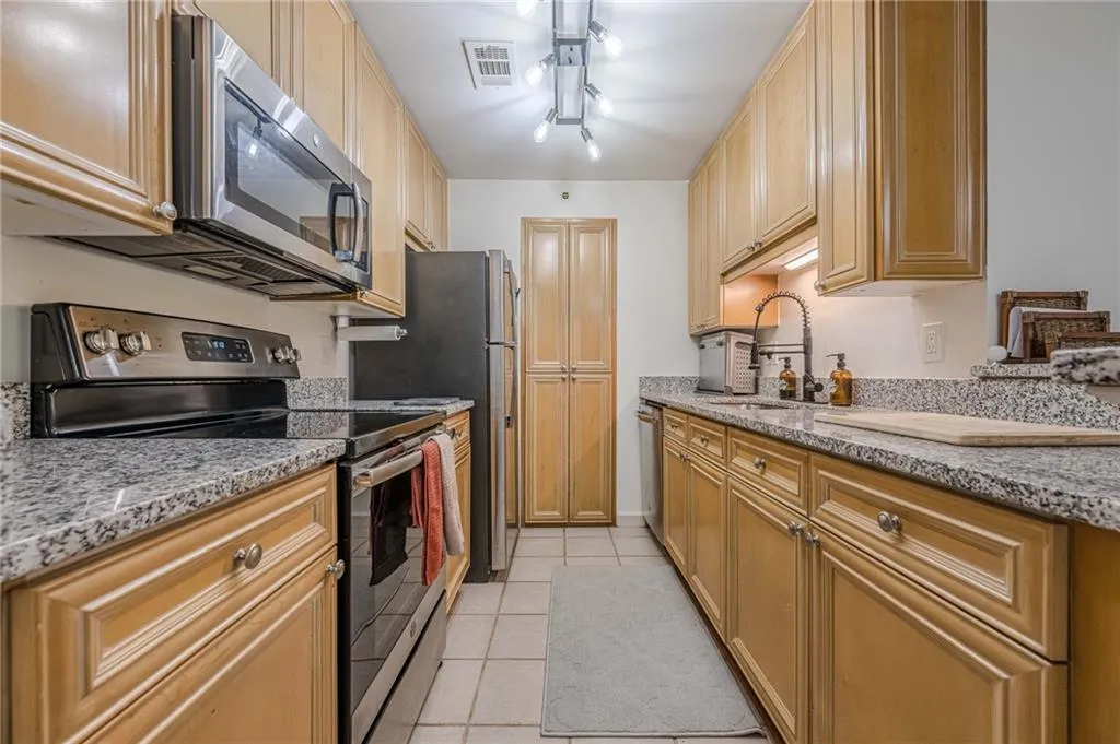 Kitchen featuring stainless steel appliances, light stone counters, light tile patterned floors, and light brown cabinetry