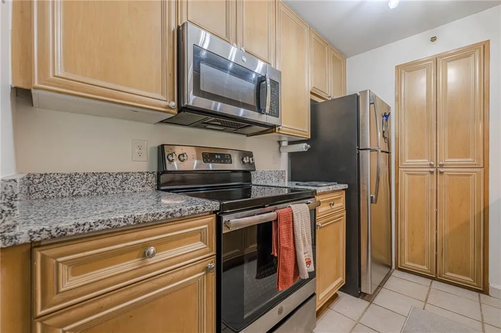 Kitchen featuring stainless steel appliances, light stone counters, light tile patterned floors, and light brown cabinets