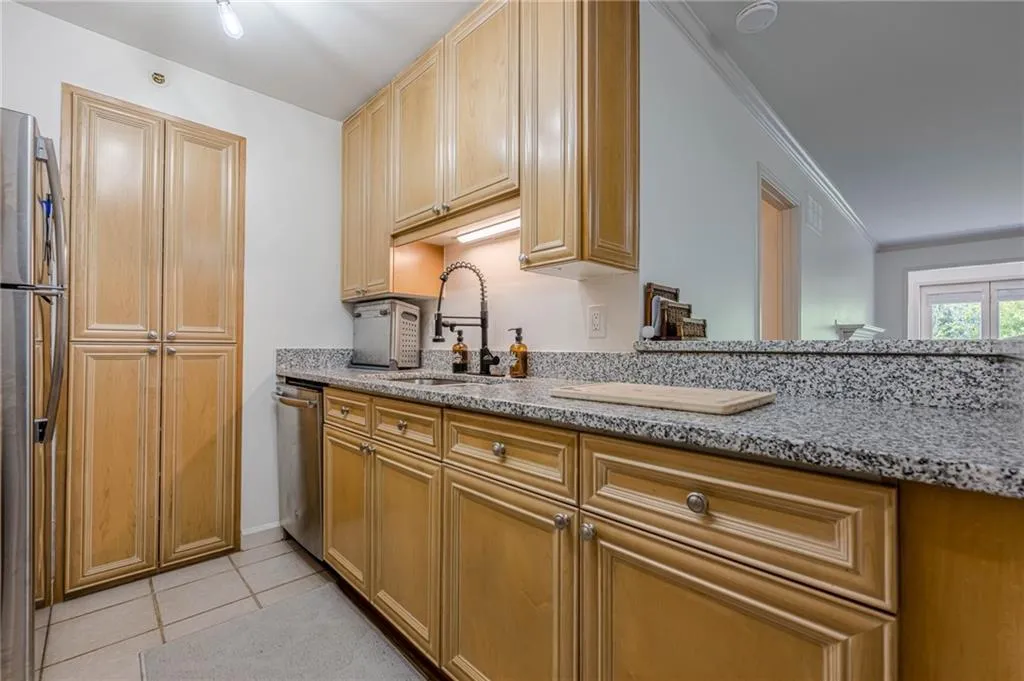 Kitchen with light stone counters, light tile patterned floors, appliances with stainless steel finishes, and crown molding
