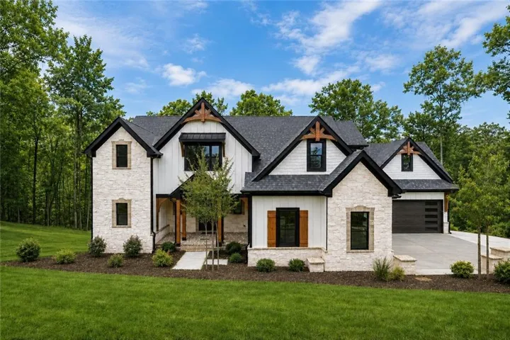 Modern farmhouse exterior featuring white board and batten siding, stone accents, black-framed windows, a dark shingle roof, and a two-car garage with a dark wood-finish door