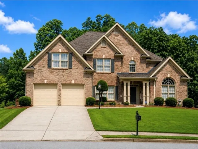 Brick facade residence featuring a covered front entry with columns, a two-car garage with light-colored doors, a concrete driveway, and mature landscaping