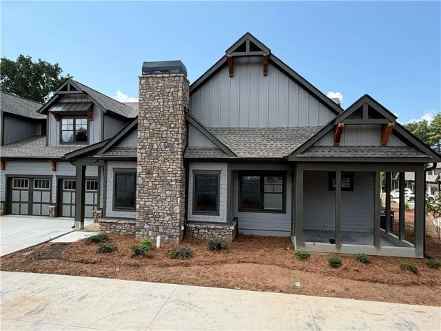 Stone chimney with metal cap, covered porch with dark wood posts, dark-framed windows, and board and batten siding