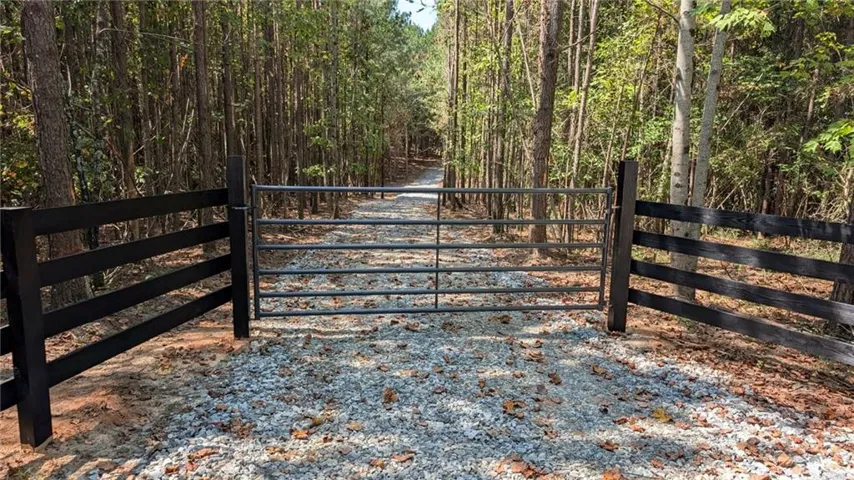 Gated gravel driveway entrance framed by a black wooden fence and mature trees