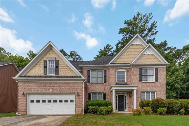 Charming two-story brick Colonial featuring a peaked gable roofline, white-trimmed windows with black shutters, and a two-car garage with white paneled doors