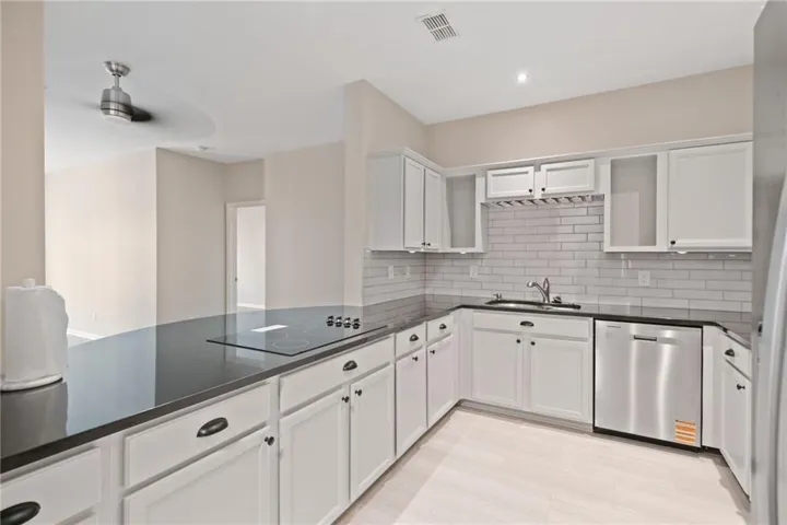 Kitchen featuring white shaker-style cabinetry, black countertops, stainless steel sink, subway tile backsplash, and wood-finish flooring