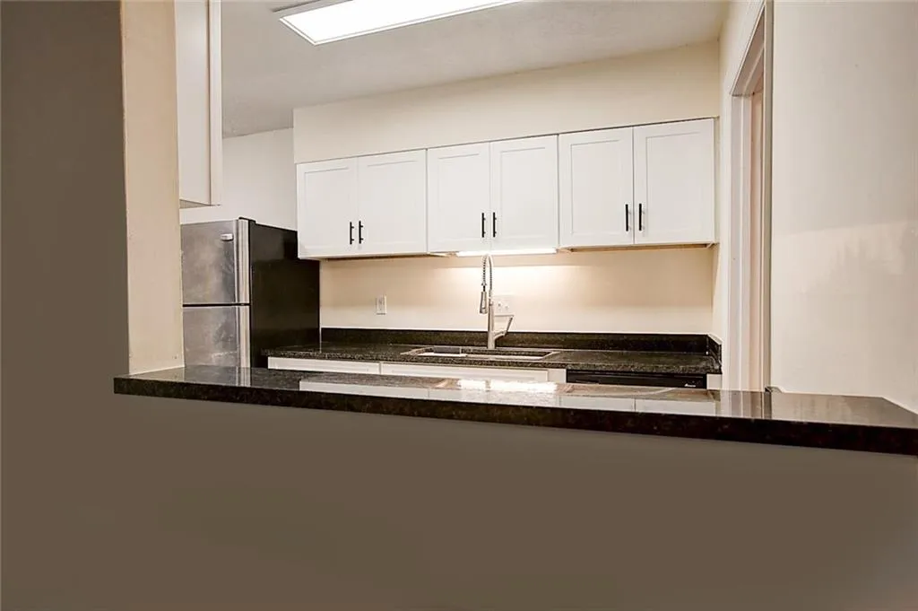 Kitchen featuring white cabinets, sink, stainless steel fridge, and dark stone countertops