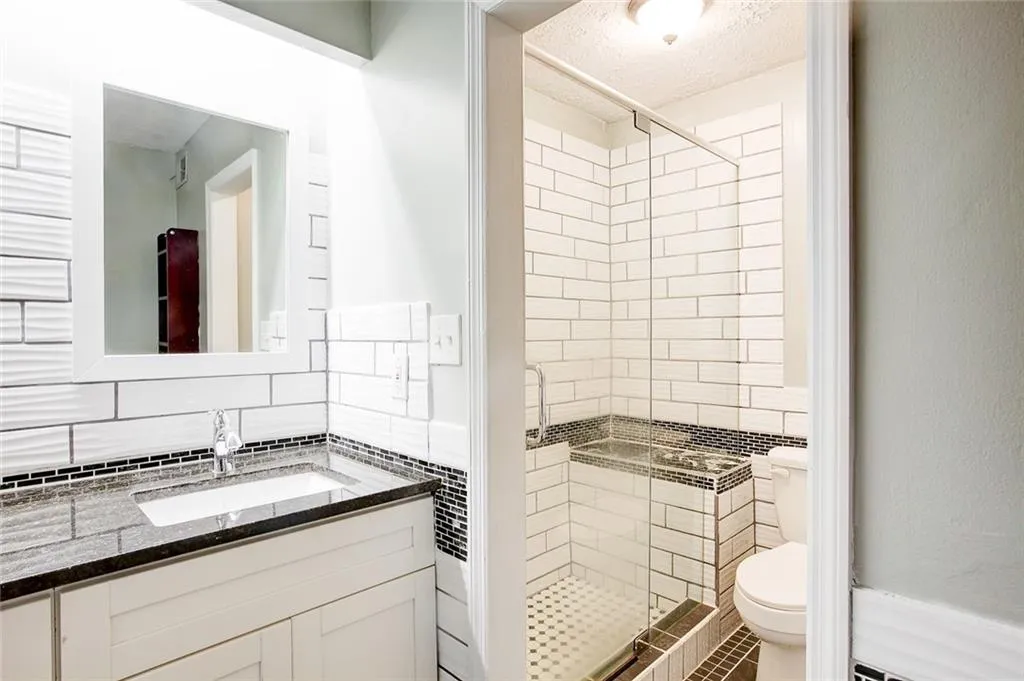 Bathroom featuring walk in shower, vanity, backsplash, and toilet