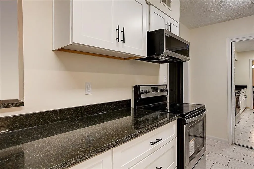 Kitchen with dark stone counters, stainless steel appliances, white cabinets, and light tile floors