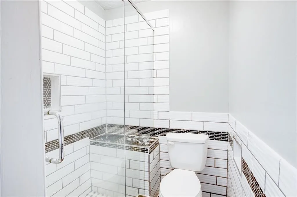Bathroom with a shower with shower door, toilet, and tile walls