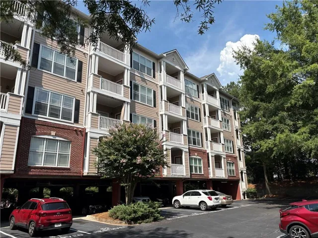Multi-story building featuring brick and siding construction, individual balconies, white railings, and covered parking