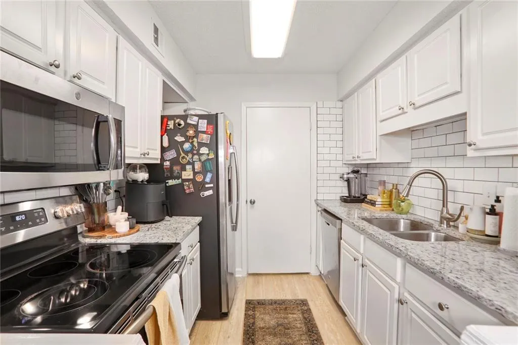 Kitchen featuring appliances with stainless steel finishes, a sink, light wood finished floors, white cabinets, and decorative backsplash