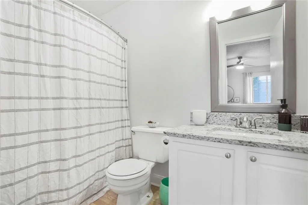 Bathroom featuring toilet, wood finished floors, vanity, a ceiling fan, and curtained shower