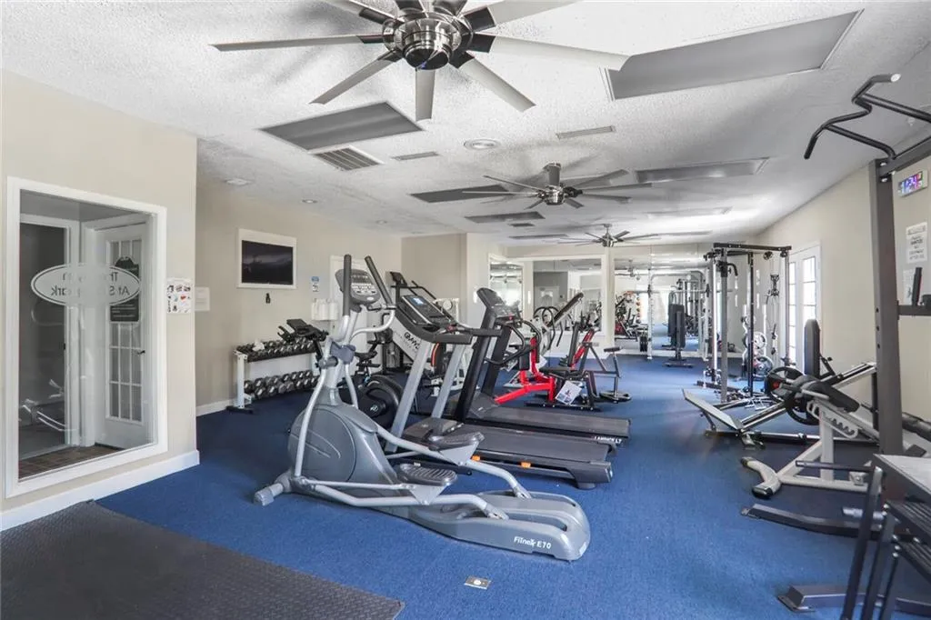 Exercise room with a ceiling fan, a textured ceiling, and baseboards