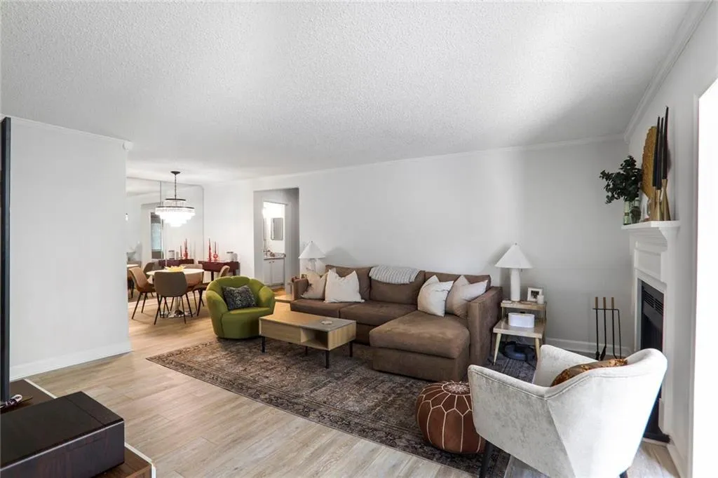 Living area featuring a textured ceiling, light wood-type flooring, crown molding, a fireplace, and baseboards