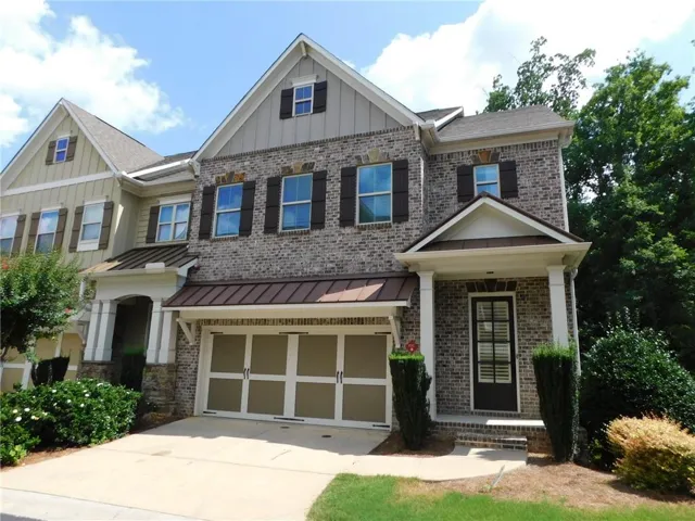 Brick and siding exterior featuring dark shutters, a two-car garage, covered entry with white columns, and mature landscaping