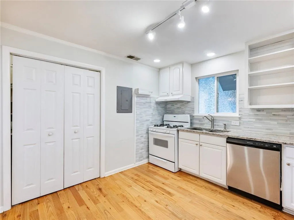 Kitchen with open shelves, white gas range oven, white cabinetry, stainless steel dishwasher, and light wood-style floors