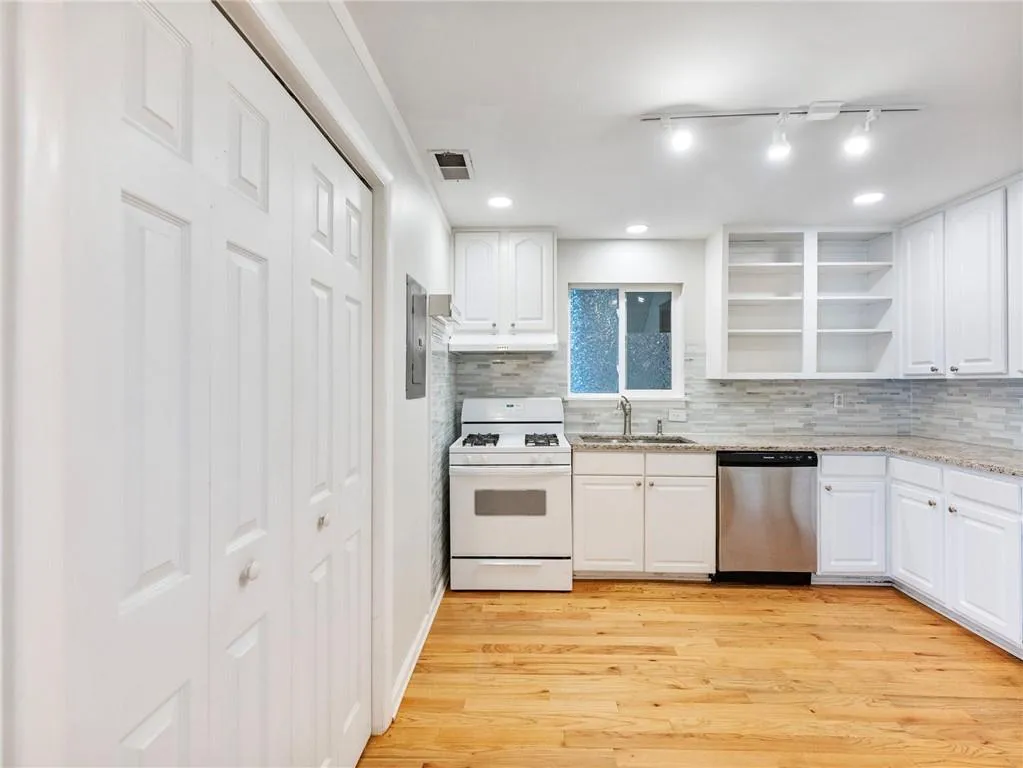 Kitchen featuring open shelves, gas range gas stove, light stone counters, stainless steel dishwasher, and light wood-style floors