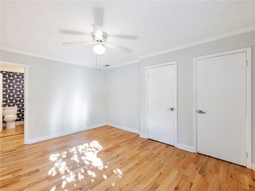 Unfurnished bedroom with ornamental molding, light wood finished floors, ceiling fan, and multiple closets