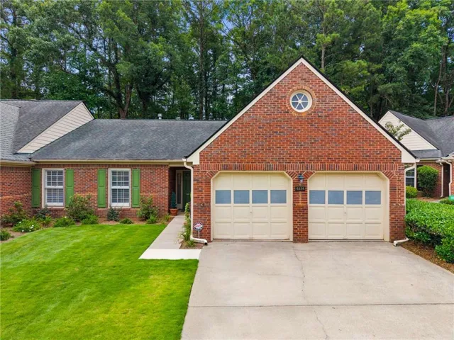 Brick exterior with a gabled roofline, featuring two garage with window panels, a prominent round accent window, and a concrete driveway