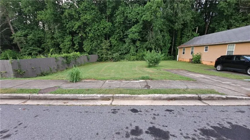 Front yard with mature trees, green lawn, and a paved driveway leading to a single-story residence
