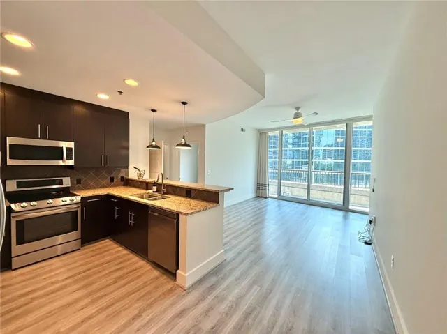 Modern kitchen featuring dark wood cabinetry, stainless steel appliances, granite countertops, and a diamond-patterned tile backsplash